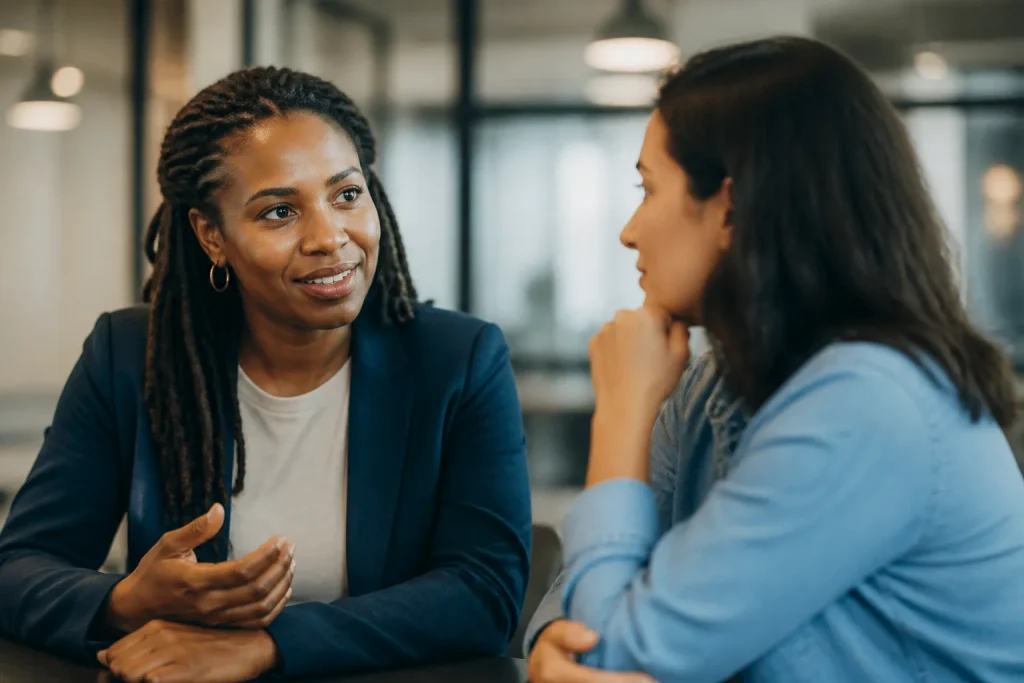 Two professionals engaged in a warm conversation at a modern office, highlighting trust-building and leadership in a relaxed setting.